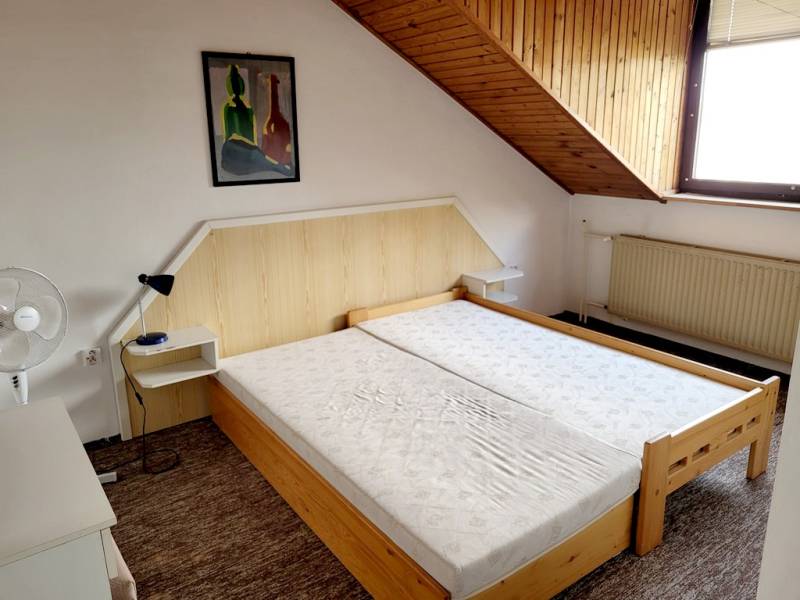 Dvoulůžková postel pod šikmým stropem v 2pokojovém bytě s obrazem na stěně.
