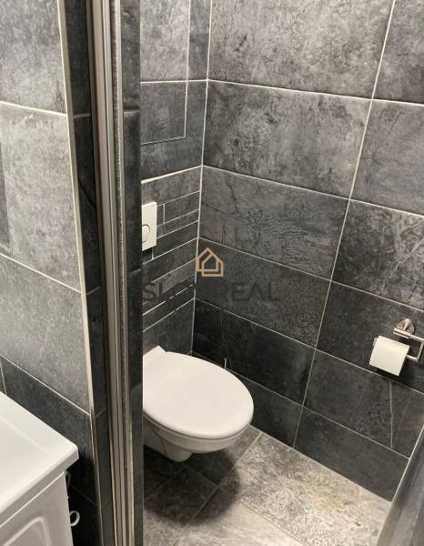 Koupelna ve 4-pokojovém bytě s tmavě šedými obklady a toaletou.