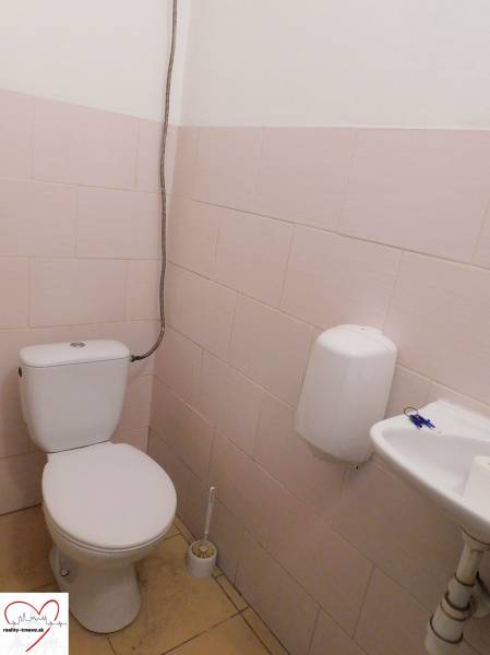 Toaleta s toaletou, umyvadlem a dávkovačem mýdla v průmyslové budově.