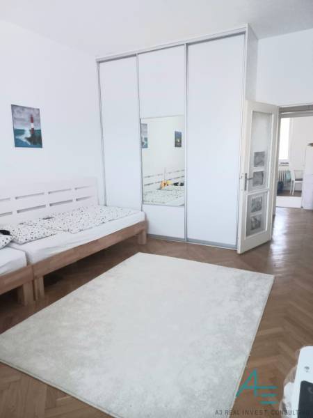 Světlá ložnice s velkou skříní a dřevěnou postelí ve 4-pokojovém bytě.