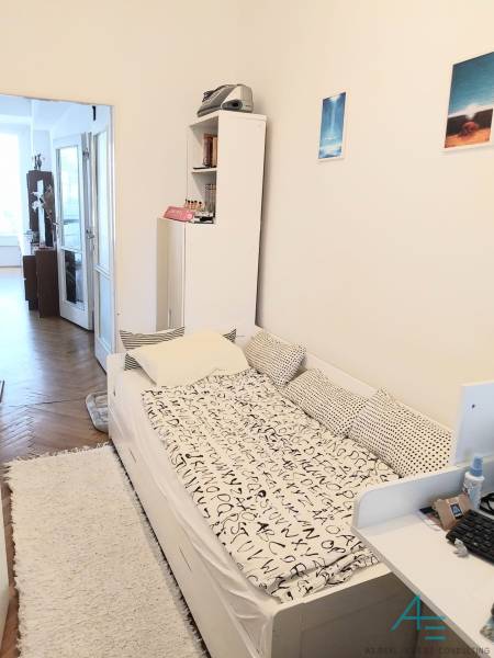 Pokoj ve 4pokojovém bytě s postelí, poličkou a vstupem na balkon.