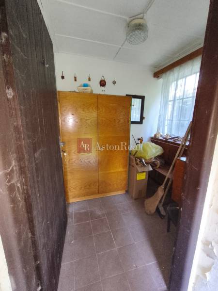 Interiér chaty s dřevěnou skříní a oknem, vedle kartonových krabic a koštěte.