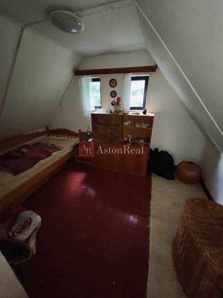 Podkrovní pokoj v chatě s postelí, skříňkou a podlahou s dřevěným dekorem.