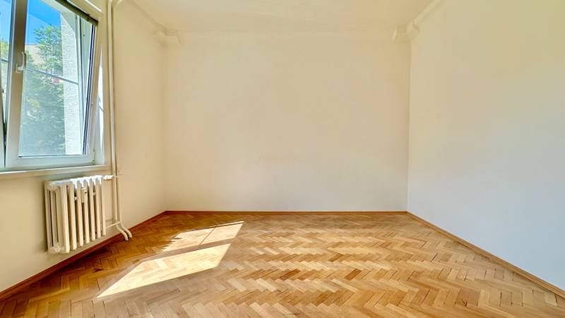 Prázdná místnost s dřevěnou podlahou a velkým oknem ve 3-pokojovém bytě.