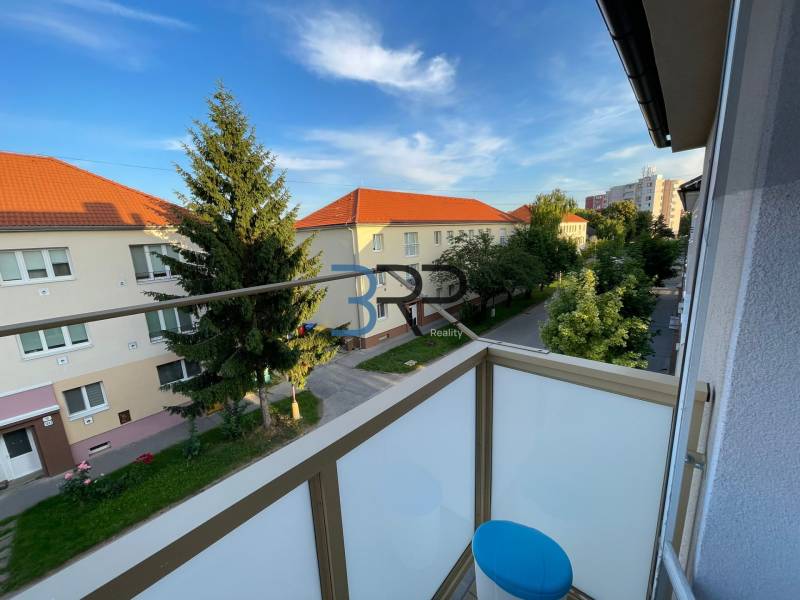 Balkon 2-pokojového bytu na Hurbanově ulici ve Skalici s výhledem na stromy a budovy.