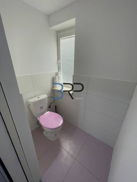 Koupelna v 2-pokojovém bytě s růžovým záchodem a bílým obkladem.