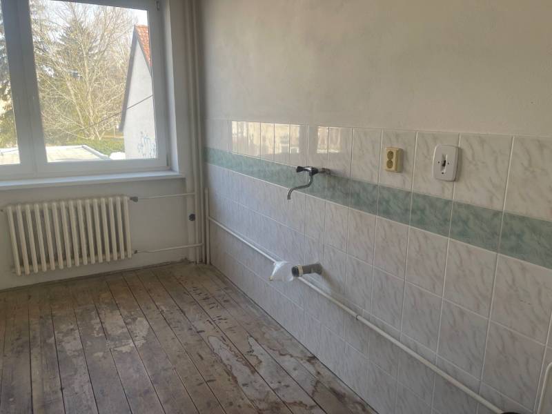 Prázdná kuchyně v rodinném domě s dlaždicemi a dřevěnou podlahou.