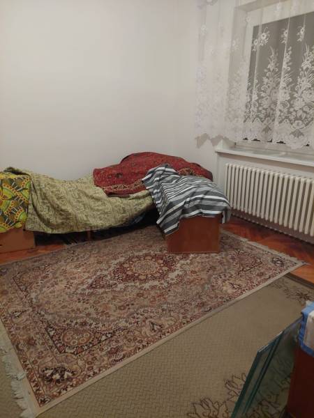 Pokoj v rodinném domě s postelí, kobercem a krajkovými záclonami.