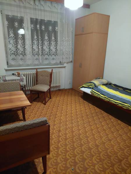 Pokoj rodinného domu s postelí, skříní, stolem a židlemi, laděný v teplých barvách.
