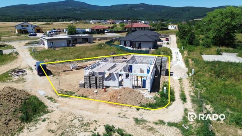 Stavba rodinného domu v Trenčianském Jastrabí, obklopená venkovskou krajinou a sousedními domy.