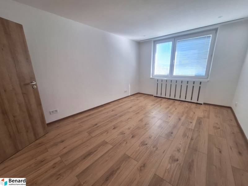 Prostorný pokoj s dřevěnou podlahou a velkým oknem v 2-pokojovém bytě.