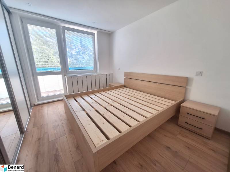 Světlá ložnice s dřevěnou postelí a nočními stolky v 2pokojovém bytě.