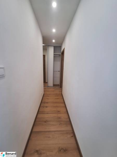 Úzká chodba s dřevěnou podlahou a vestavěnou skříní v 2-pokojovém bytě.