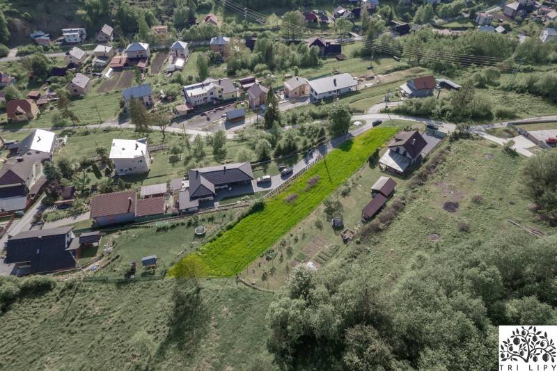 Letecký pohled na obytné pozemky v obci Raková, zelené svahy a domy.
