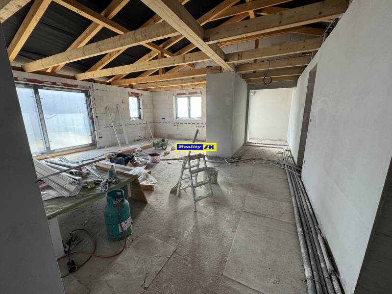 Stavba v rodinném domě s odkrytými nosníky a stavebním materiálem na podlaze.