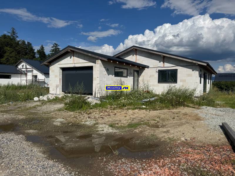 Nedokončený rodinný dům ve Valči s garáží obklopený přírodou a stavebním materiálem.
