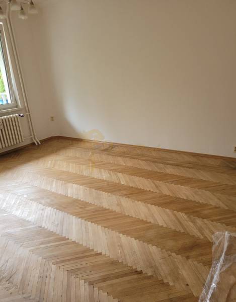 Prázdný pokoj v třípokojovém bytě s parketovou podlahou a oknem.