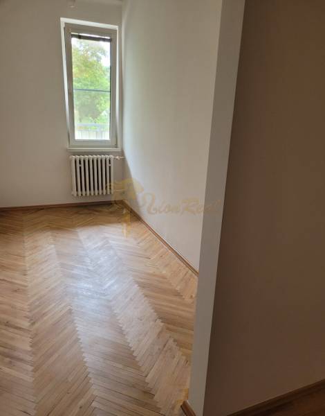Pokoj v 3-pokojovém bytě s dřevěnou podlahou a radiátorem pod oknem.