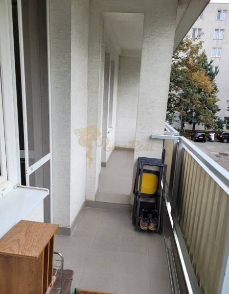 Balkon v 3-pokojovém bytě se skládacími židlemi a výhledem na stromy na dvoře.