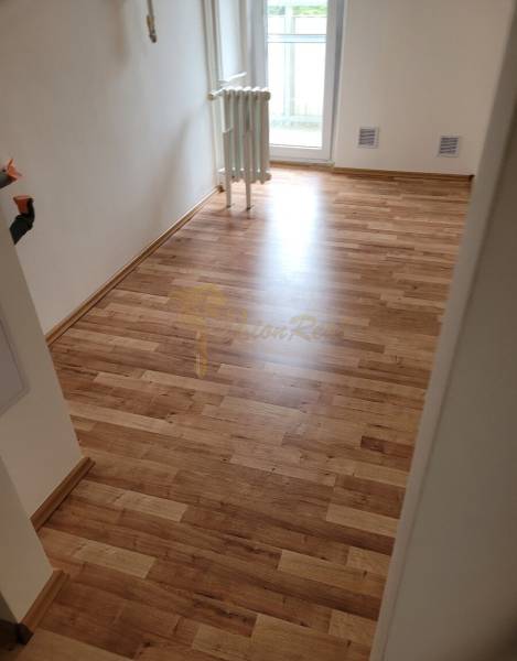 V 3-pokojovém bytě je vidět místnost s dřevěnou podlahou a radiátorem.