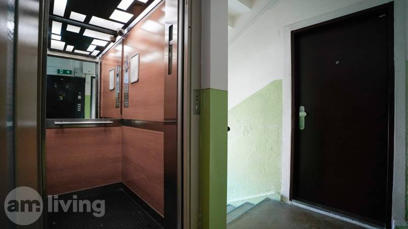 Výtah s dřevěným dekorem a schodiště s dveřmi do 2pokojového bytu.
