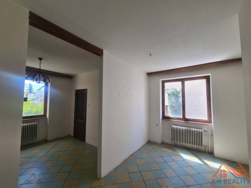 Interiér rodinného domu s kachličkovou podlahou a dřevěným trámem na stropě.