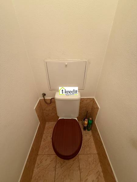 Toaleta s hnědým sedátkem a obklady v 2-pokojovém bytě.