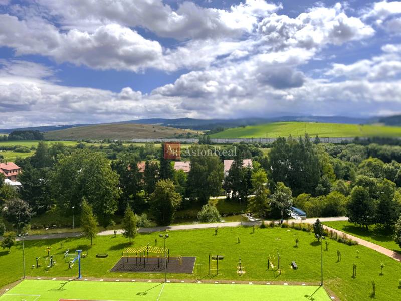 Pohled z 2-pokojového bytu na Západě v Tvrdošíně, s hřištěm a kopcovitou krajinou.