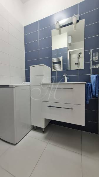 Koupelna v 2-pokojovém bytě se skříňkou, umyvadlem a zrcadlem na stěně.
