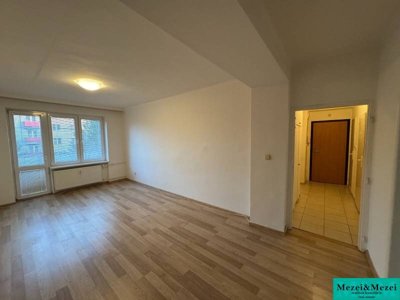 Prostorný pokoj s laminátovou podlahou v 2pokojovém bytě, sluneční světlo přes velké okno.