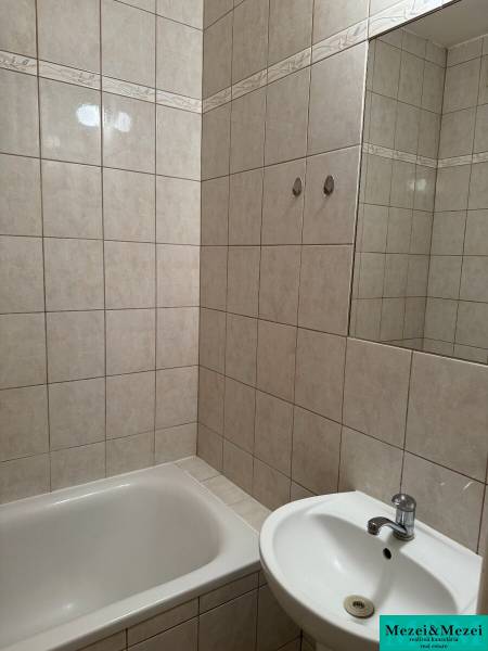 Koupelna se sprchou a umyvadlem v 2-pokojovém bytě, obložená béžovými kachličkami.