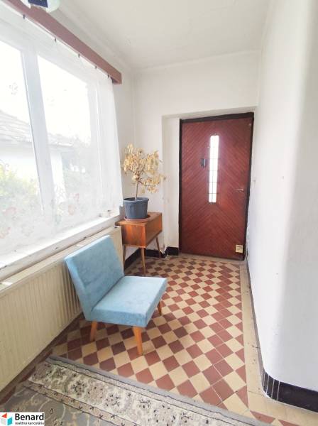 Vstupní chodba v rodinném domě s květináčem, modrou židlí a šachovnicovou dlažbou.