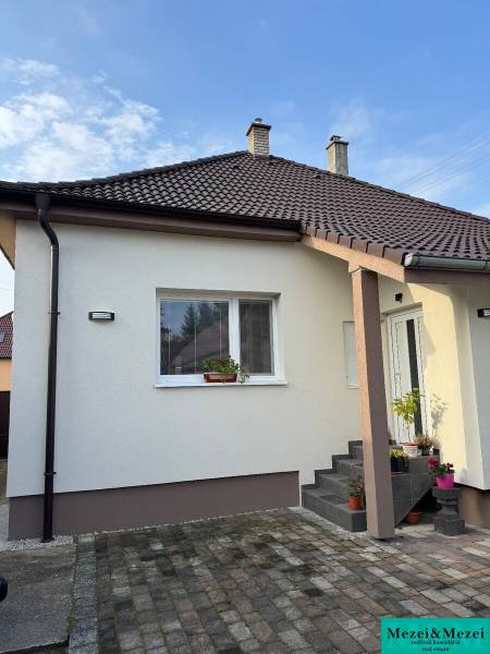 Rodinný dům v Trstíně s bílou fasádou, hnědou střechou a dlážděným chodníkem.