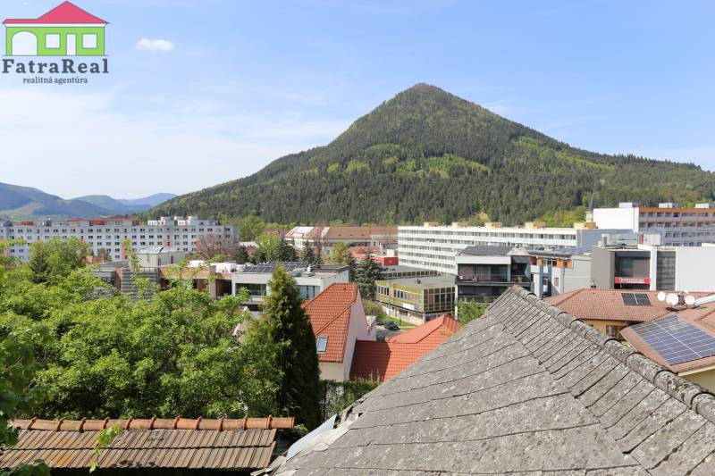 Na ulici Nám. A. Hlinku je vidět střechy, budovy a zalesněný kopec za Rodinným domem.