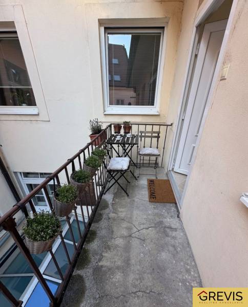 Úzký balkon s kovovým zábradlím, židlemi a květináči v 2-pokojovém bytě.