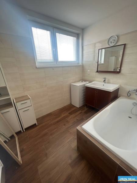 Koupelna ve 3-pokojovém bytě s vanou, zrcadlem a dřevodekorem na podlaze.