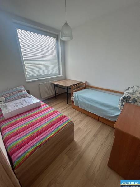 Pokoj v 3-pokojovém bytě se dvěma postelemi, stolem a dřevěnou podlahou.