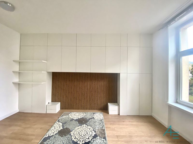 Bílá stěnová sestava s úložným prostorem a podlaha s dřevěným dekorem ve 3-pokojovém bytě.