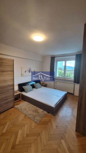 Ložnice s vestavěnou skříní, dvoulůžkem a podlahou s dřevěným dekorem v 2pokojovém bytě.