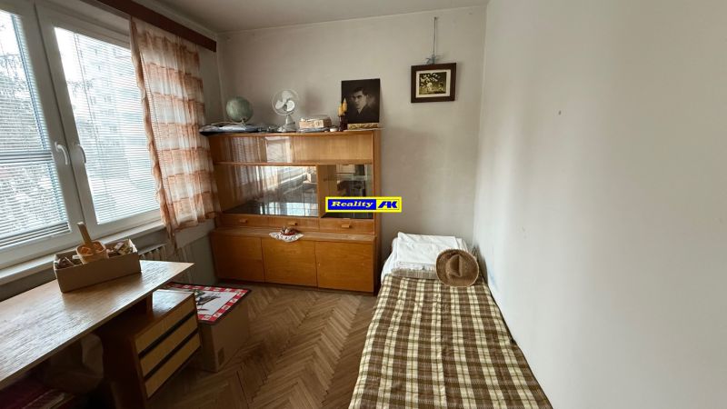 Pokoj s postelí, skříní a stolkem, v 3-pokojovém bytě s podlahou s dřevěným dekorem.
