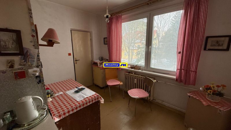 Kuchyně ve 3-pokojovém bytě s červenobílými závěsy, dřevěnou podlahou a stolem.