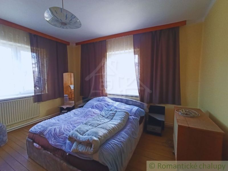 Ložnice s velkými okny, podlahou s dřevěným dekorem a postelí v rodinném domě.