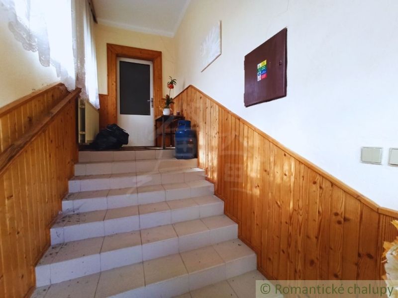 Schodiště v rodinném domě s dřevěným obkladem a keramickými dlaždicemi na schodech.
