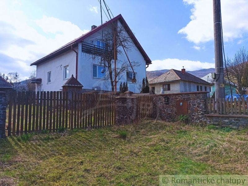 Rodinný dům v obci Zboj se zahradou a dřevěným plotem na pozadí hor.