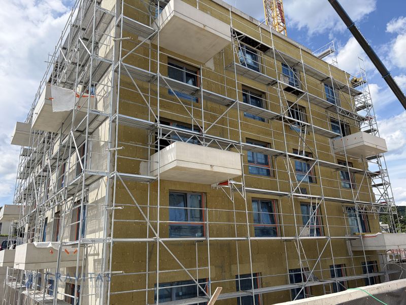 Budova v Bratislavě - Rači během rekonstrukce, obklopená lešením a s viditelnými balkony.