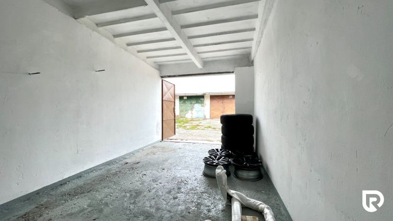 V garáži jsou pneumatiky a ráfky, betonová podlaha, studené bílé stěny.