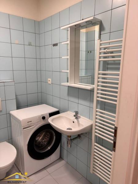 Koupelna v 1-pokojovém bytě s pračkou a umyvadlem, světle modré obklady.