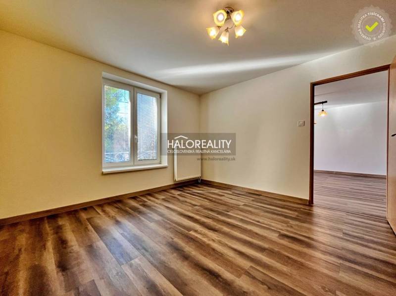 Pokoj v 3-pokojovém bytě s podlahou s dřevěným dekorem a velkým oknem.