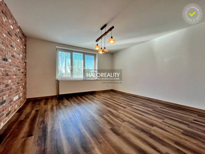 Pokoj ve 3-pokojovém bytě s podlahou s dřevěným dekorem a cihlovým obkladem na stěně.