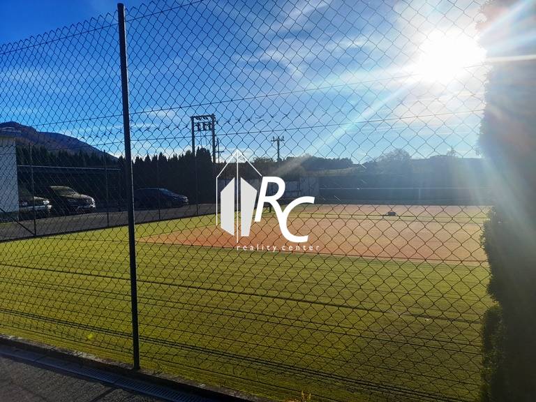 Tenisový kurt u rodinného domu v Necpalech, oplocený a osvětlený slunečními paprsky.